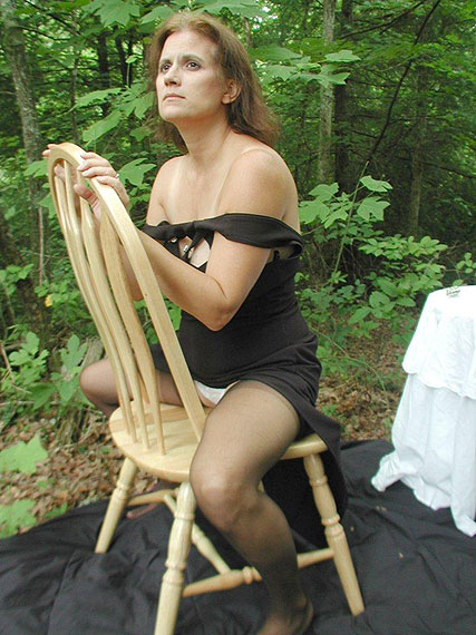 Ältere Frau sitzt auf einem Stuhl draußen im Wald